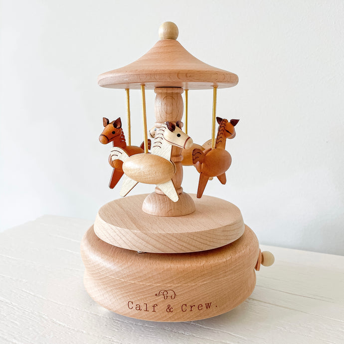 a wooden musical carousel with spinning horses and the calf & crew logo engraved on the bottom