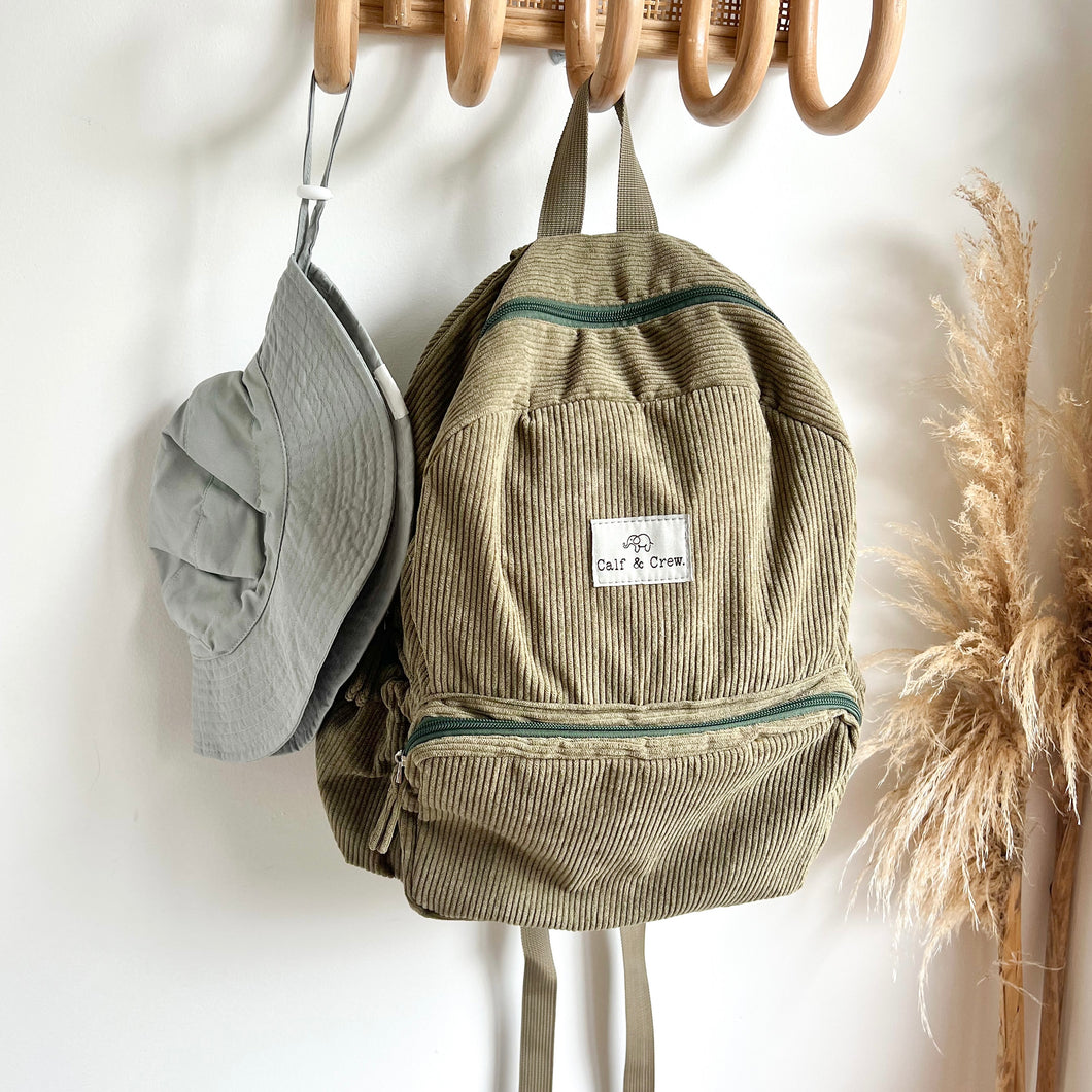 a everyday sunhat in cloudy blue hanging on a wooden hook with a khaki coloured corduroy backpack
