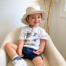 Load image into Gallery viewer, child sitting in a soft white chair wearing the sun hat in sand colour

