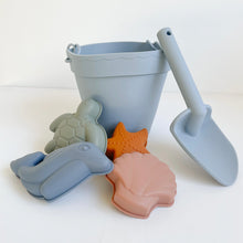 Load image into Gallery viewer, the silicone beach toy set in ocean colour showing blue bucket and spade, and shape moulds of a green turtle, blue dolphin, orange starfish and pink seashell
