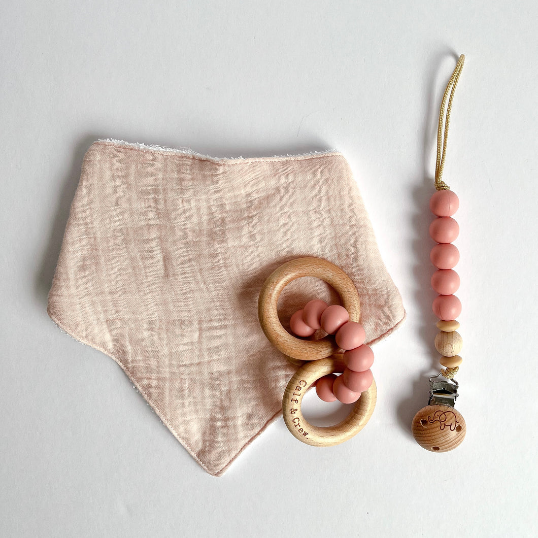 Baby pink coloured muslin bib with a wooden silicone ring teether and silicone dummy clip in blush