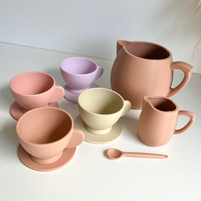 the silicone toy tea set in sunrise colour showing the four different coloured teacups & saucers, a peach coloured milk jug, stirring spoon, and teapot