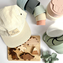 Load image into Gallery viewer, A crew cap in cream colour, silicone stacking cups spilled to the side, a wooden dinosaur puzzle, and a collapsible snack cup and easy grip spoon and fork in sage colour
