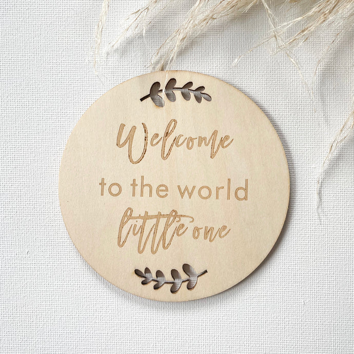 a wooden disc with leaf cutouts and Welcome to the world little one engraved