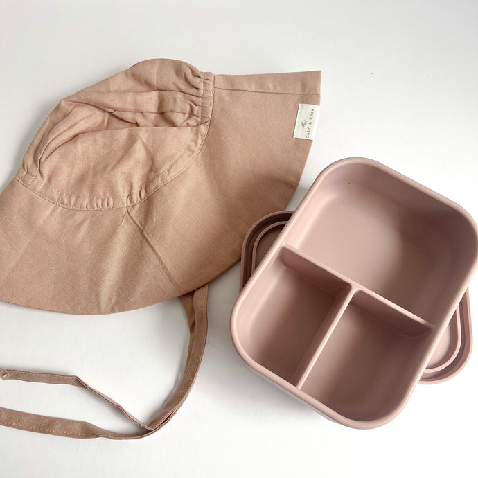 a folded floppy sun hat in rose colour with a open silicone bento lunchbox in rose colour