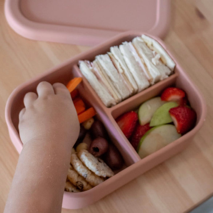 a hand reaching into a rose silicone bento lunchobox grabbing a variety of food