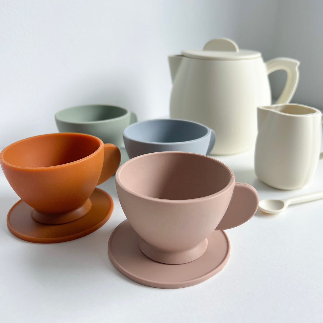 the silicone toy tea set in snow colour showing 4 different coloured tea cups & saucers, and a white milk jug, stirring spoon, and teapot