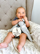 Load image into Gallery viewer, a baby sitting on a grey chair with the 4 month wooden milestone disc
